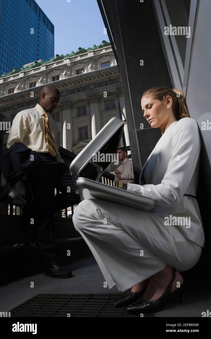 Vista ad angolo basso di una donna d'affari che guarda in una valigetta con due uomini d'affari in piedi sullo sfondo Foto Stock