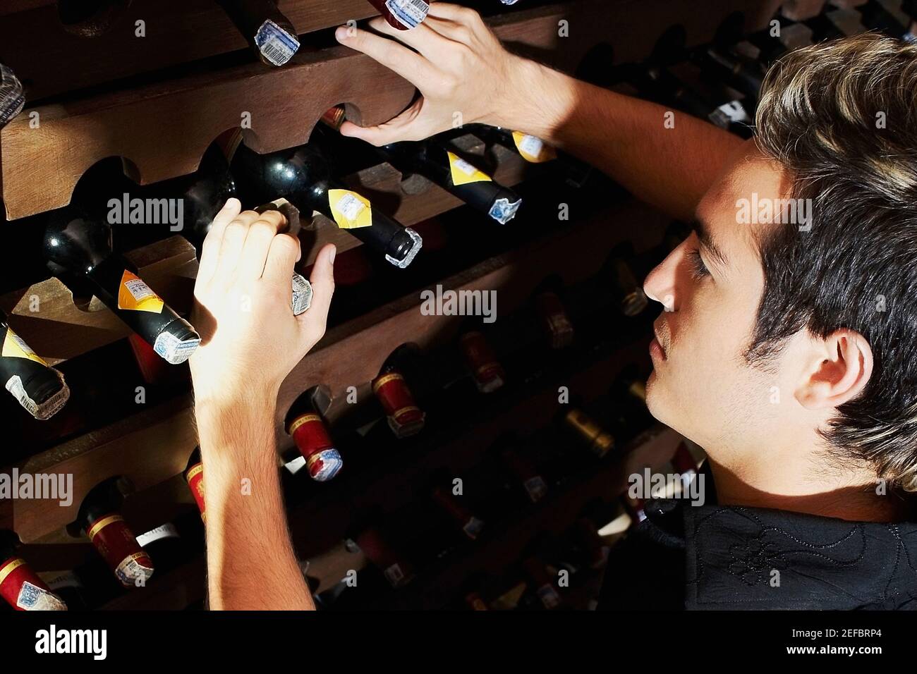 Profilo laterale di un giovane da cui prende una bottiglia una rastrelliera per vini Foto Stock