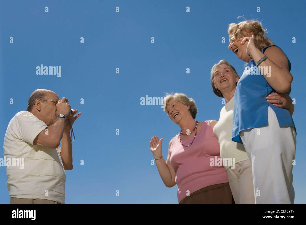 Vista ad angolo basso di un uomo anziano che fotografa tre donne anziane Foto Stock