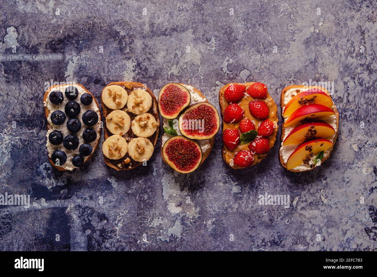 Toast estivi fatti in casa con formaggio cremoso, burro di noci, frutta e bacche, vista dall'alto. Foto Stock