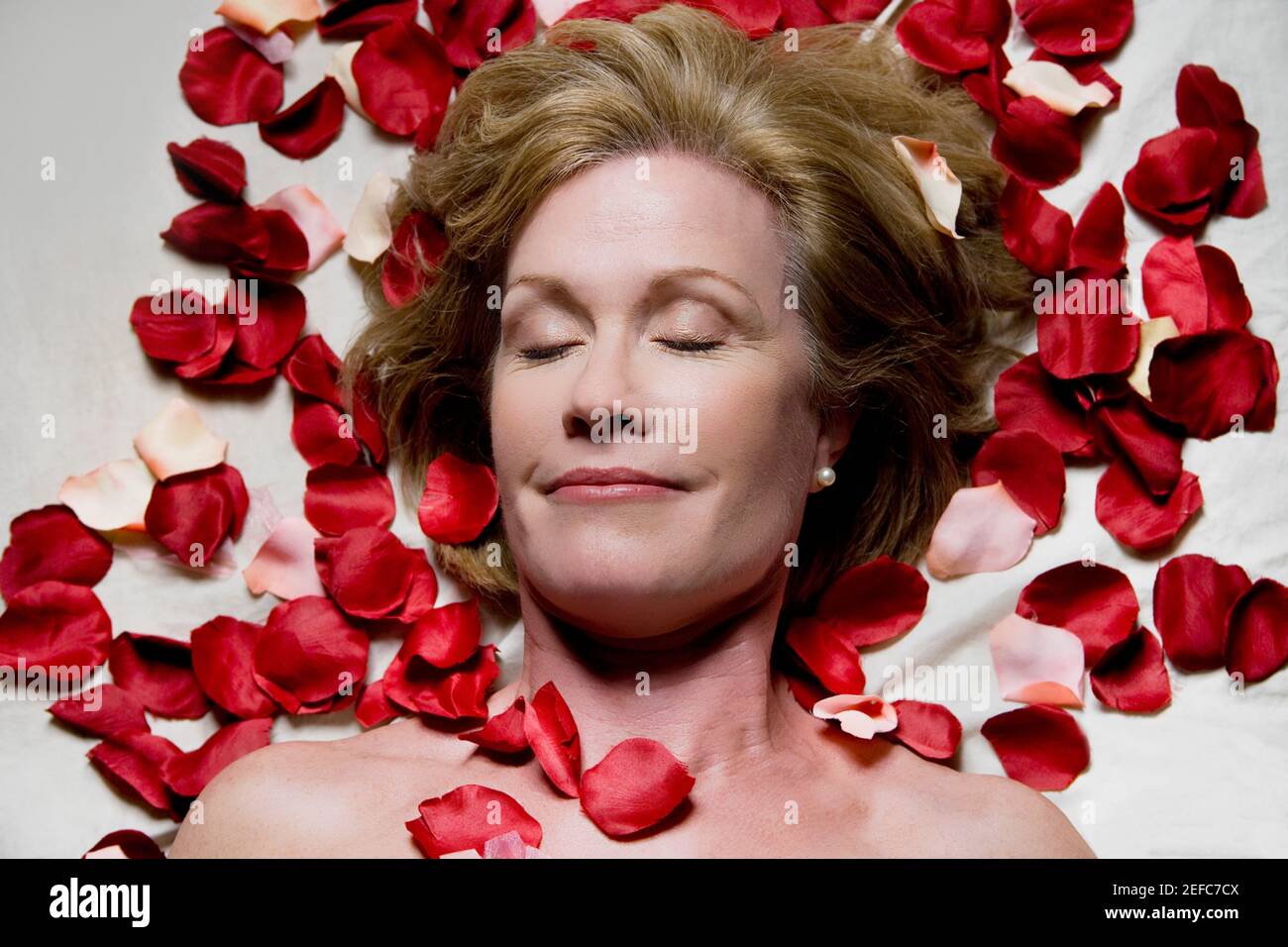 Vista ad alto angolo di una donna matura che giace su un tavolo da massaggio con petali di rosa intorno a lei Foto Stock