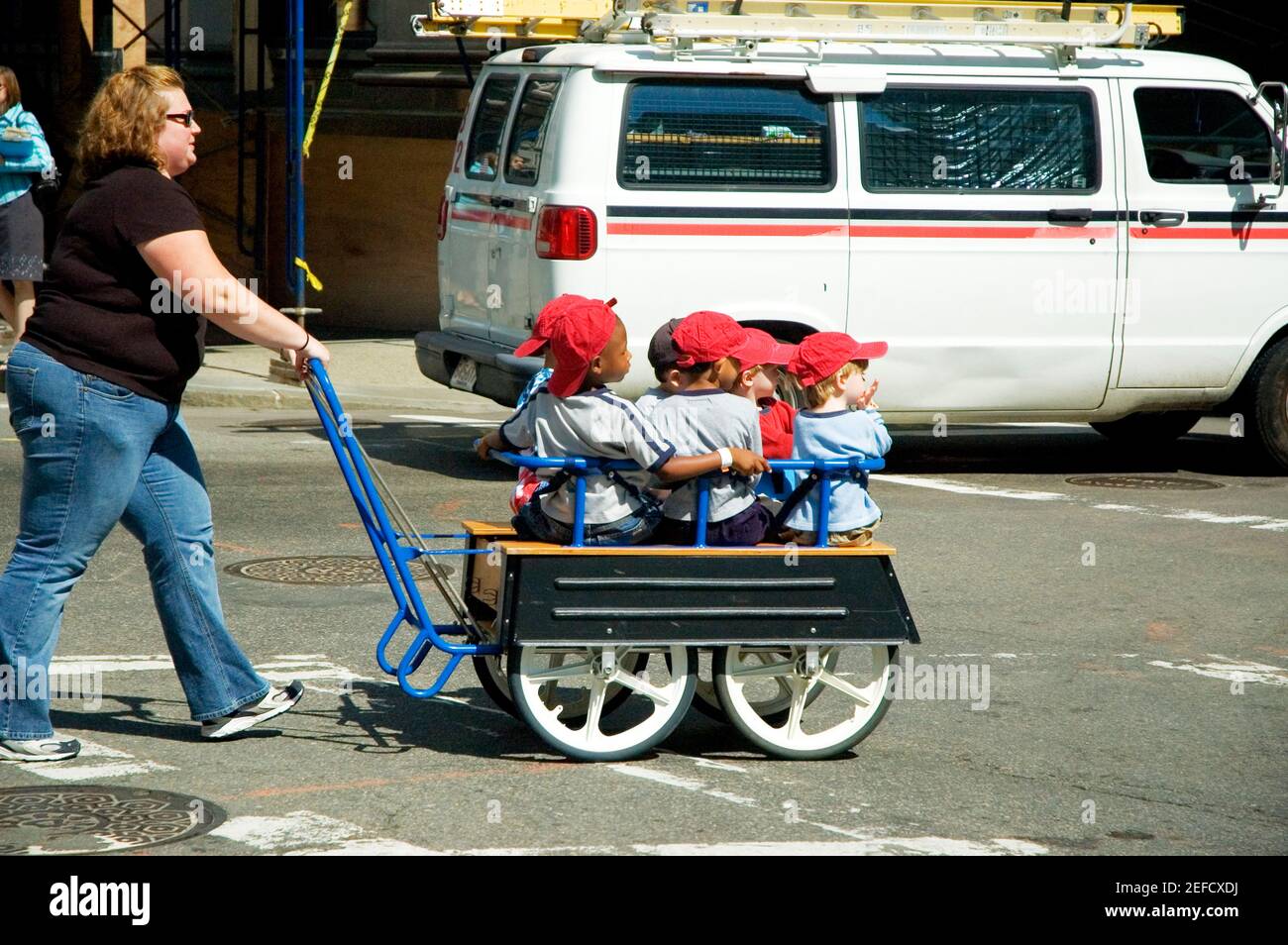 Donna mid adulta che spinge i bambini in un trolley Foto Stock