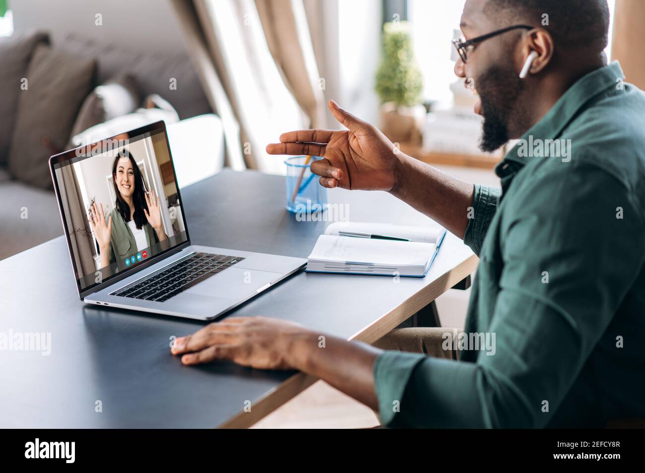 Un ragazzo afro-americano che parla con una videochiamata con una collega o una ragazza caucasica, utilizzando un'app di comunicazione online e un laptop, seduto a casa. Video meeting online Foto Stock