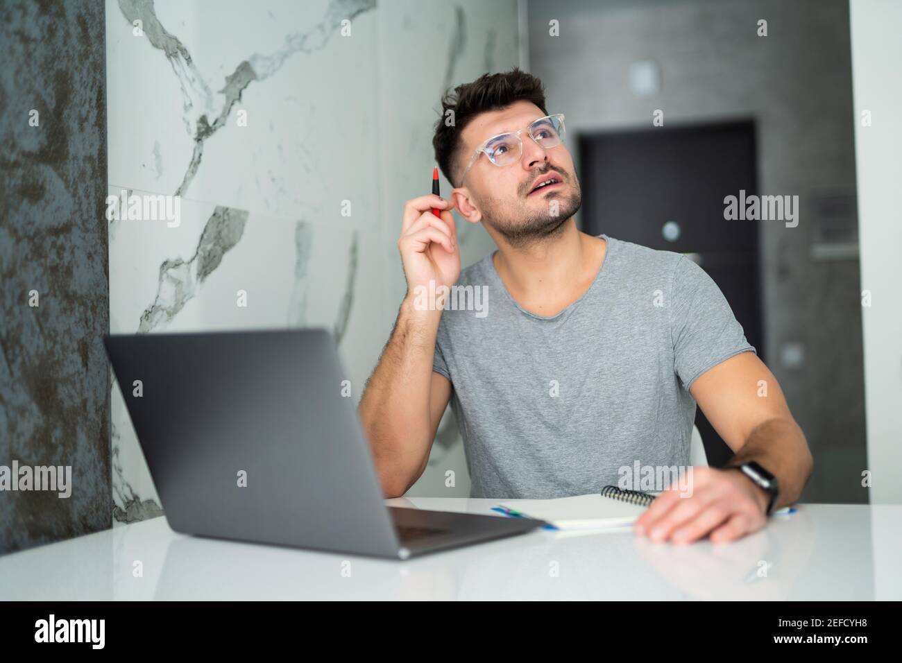 Uomo serio che indossa gli occhiali calcolando le fatture o le tasse domestiche, le spese della famiglia, usando il laptop e la calcolatrice nella cucina moderna Foto Stock