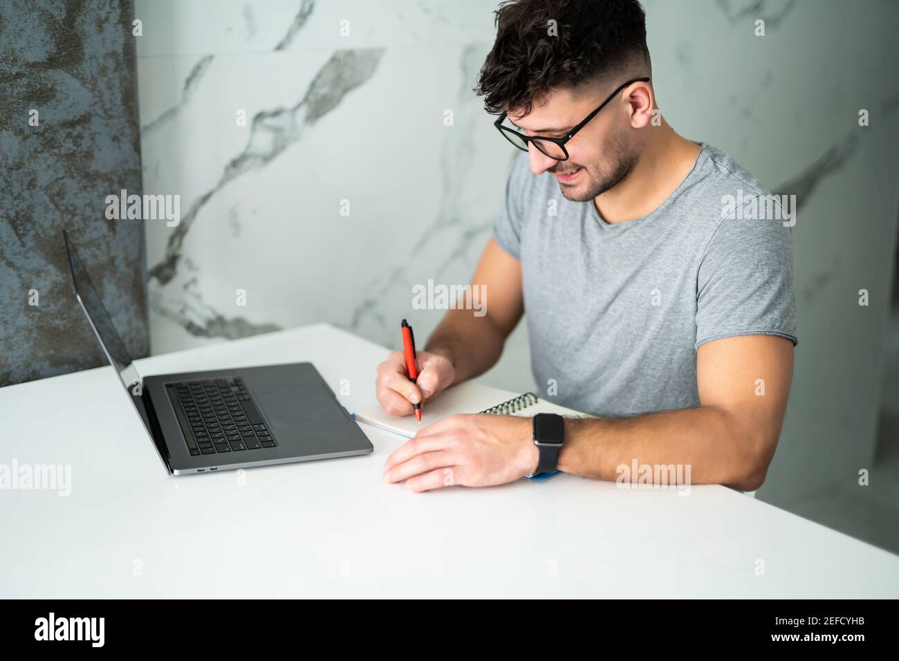 Uomo serio che indossa gli occhiali calcolando le fatture o le tasse domestiche, le spese della famiglia, usando il laptop e la calcolatrice nella cucina moderna Foto Stock