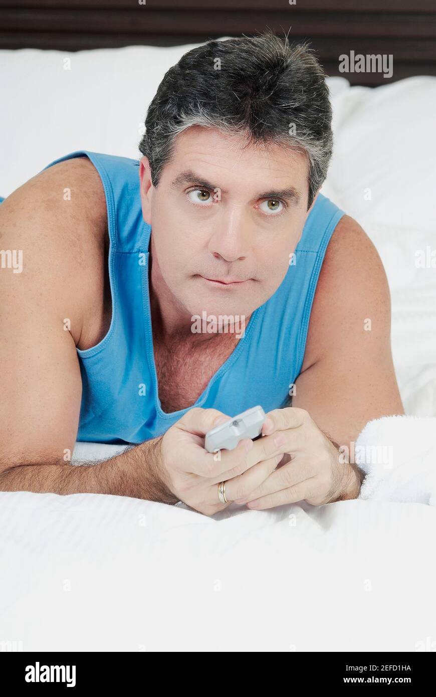Uomo maturo sdraiato sul letto e funzionante un telecomando controllo Foto Stock