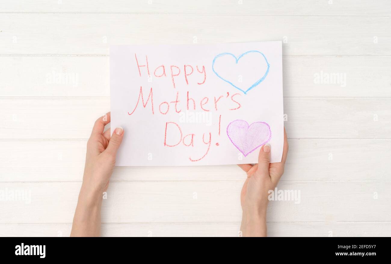 Le mani della donna che tengono la cartolina dipinta DIY per il giorno delle madri. Concetto di giorno della madre felice. Vista dall'alto Foto Stock