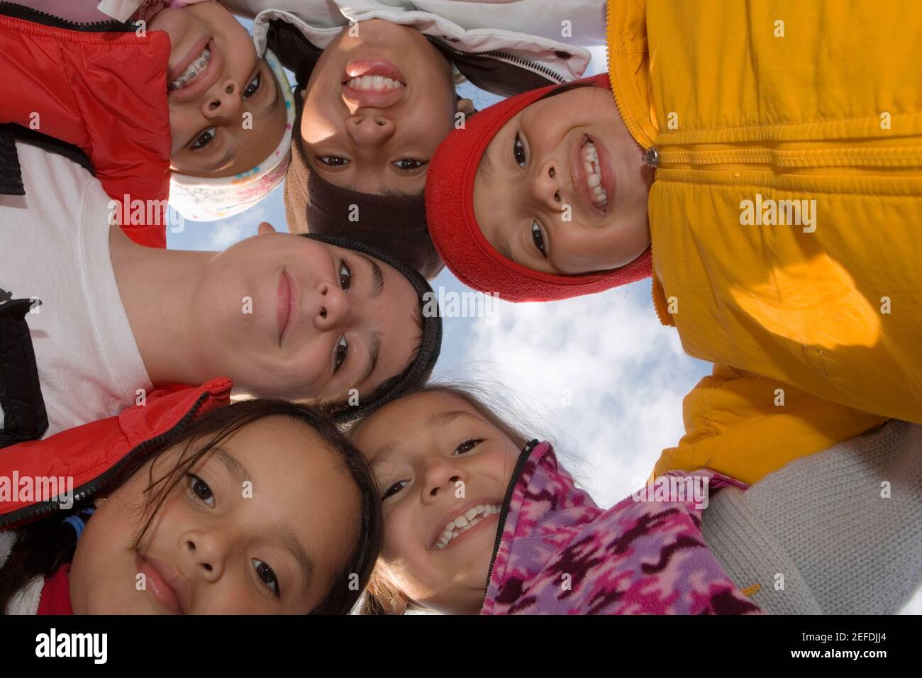 Vista ad angolo basso di cinque bambini e di un ragazzo adolescente in piedi in cerchio e sorridente Foto Stock