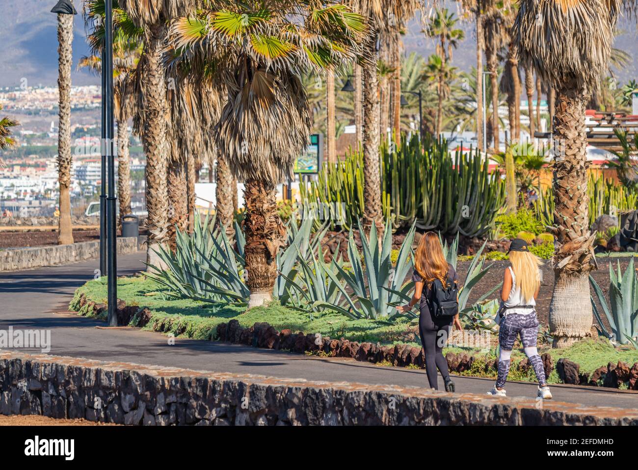 Boulevard con palme e vista posteriore di due donne a Playa de Las Americas, Tenerife, Isole Canarie Foto Stock