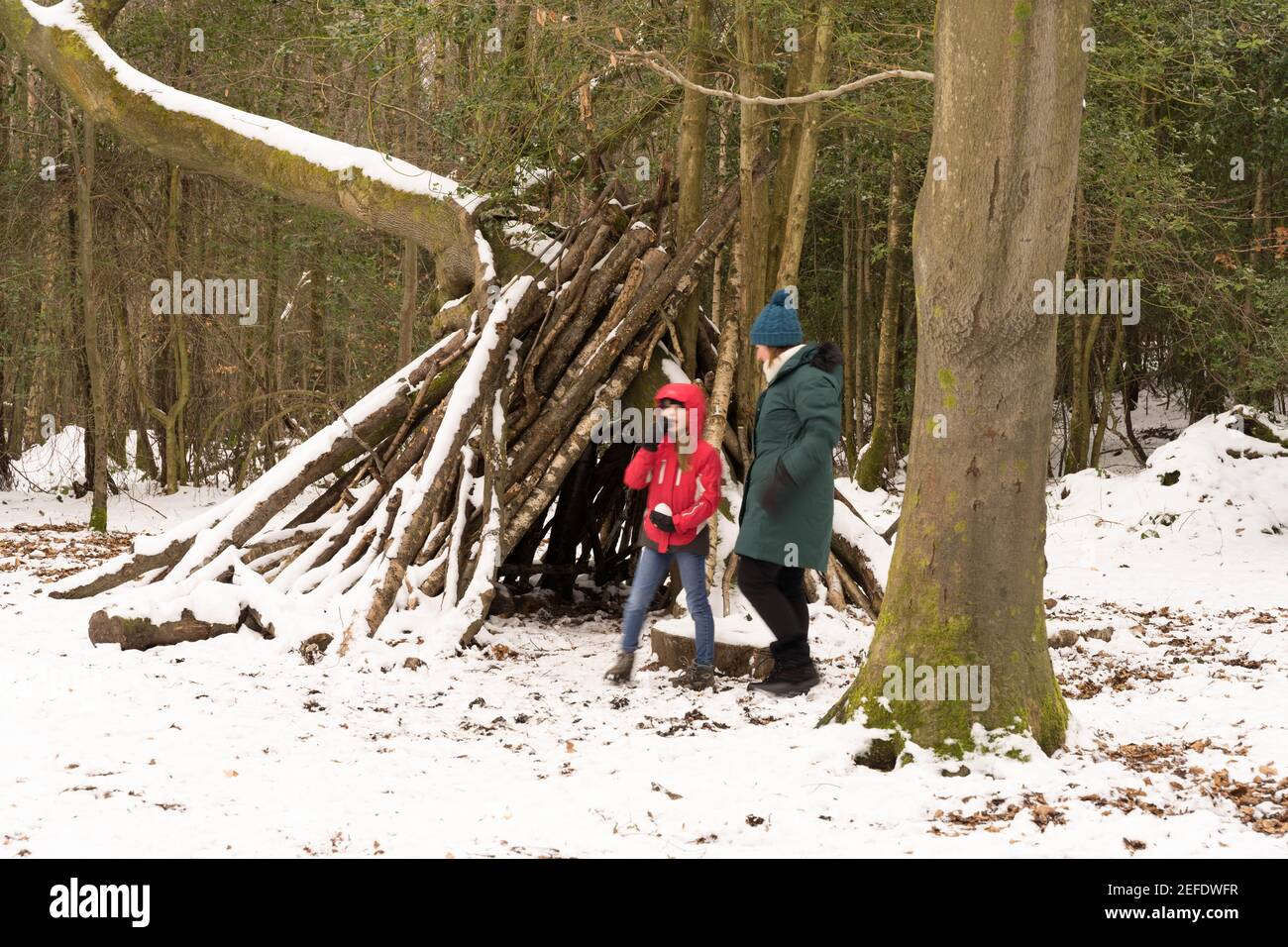 ragazzo e sua mamma si godono la neve scena circondano il capanna di alberi di bosco di ramoscelli e rami ricoperti di neve Foto Stock