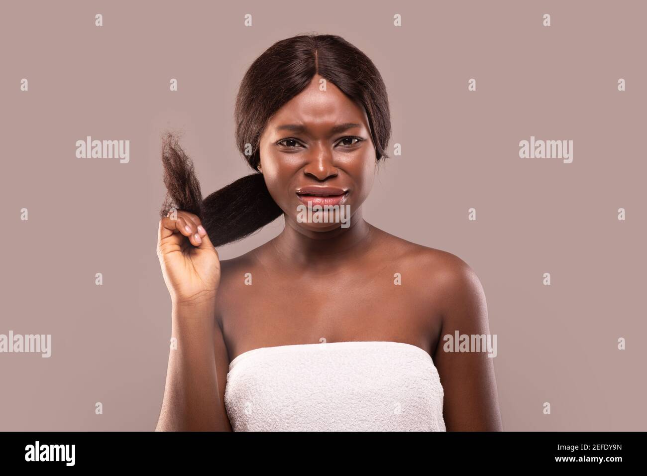 Dividi estremità. Sconvolto Afro American Woman deluso con i suoi capelli danneggiati, frustrata Black Lady accigliato mentre si guarda la fotocamera, in piedi avvolto Foto Stock