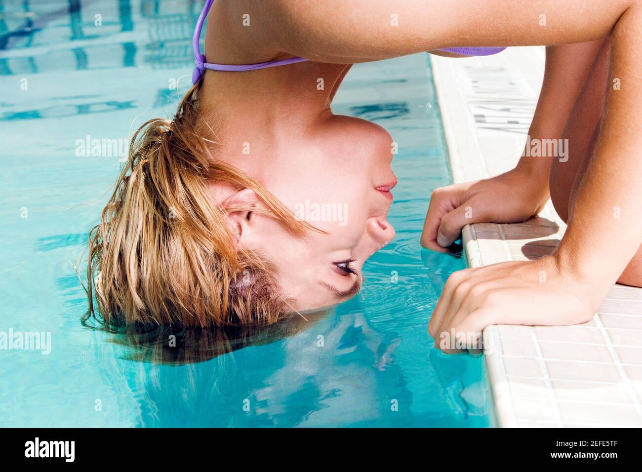 Ritratto di una giovane donna che si piega in avanti con i capelli in una piscina Foto Stock