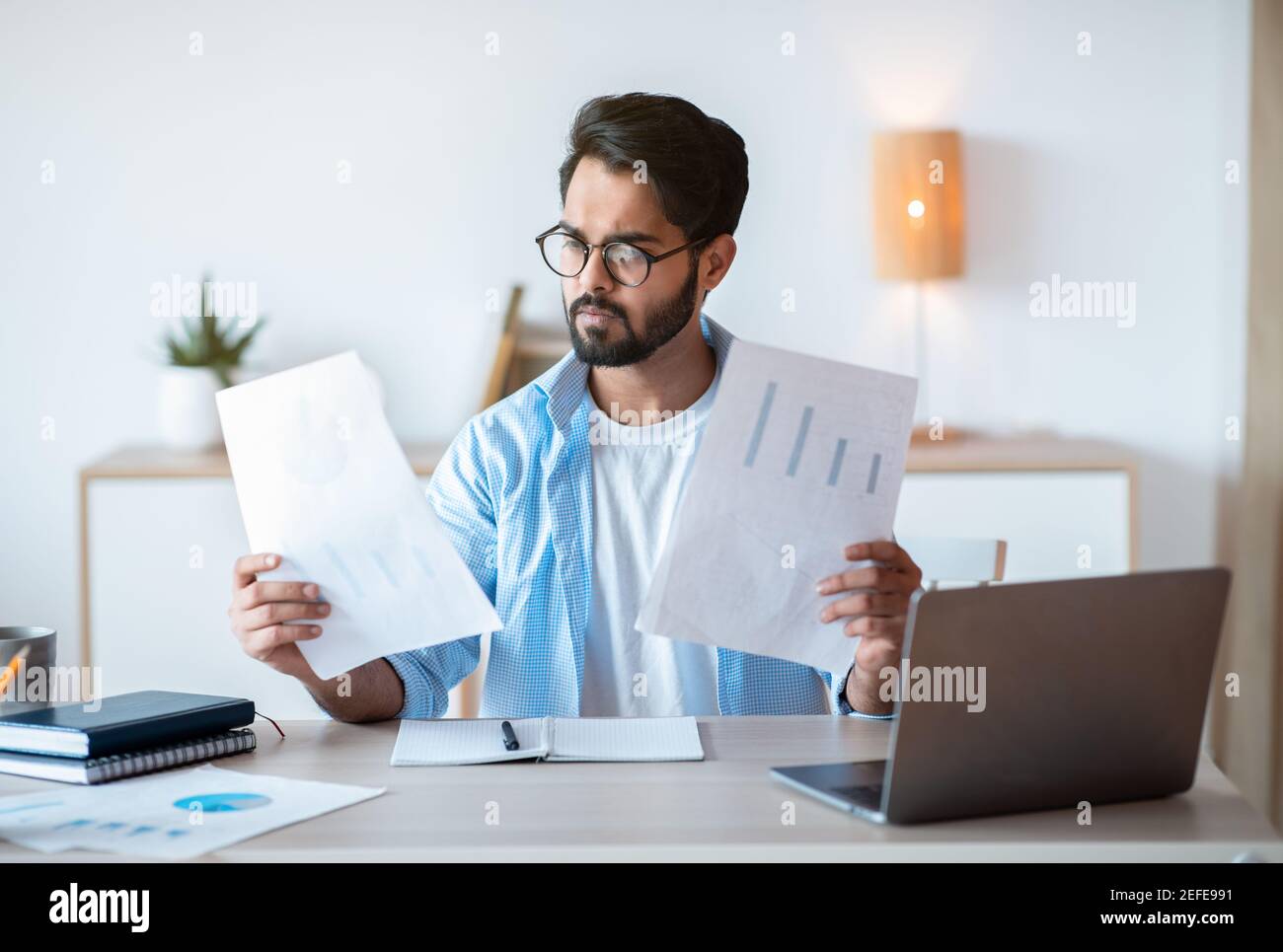 Imprenditore maschio arabo occupato che lavora con i documenti e il laptop in ufficio, uomo d'affari orientale che verifica i rapporti finanziari e che legge i documenti a Worplace Foto Stock