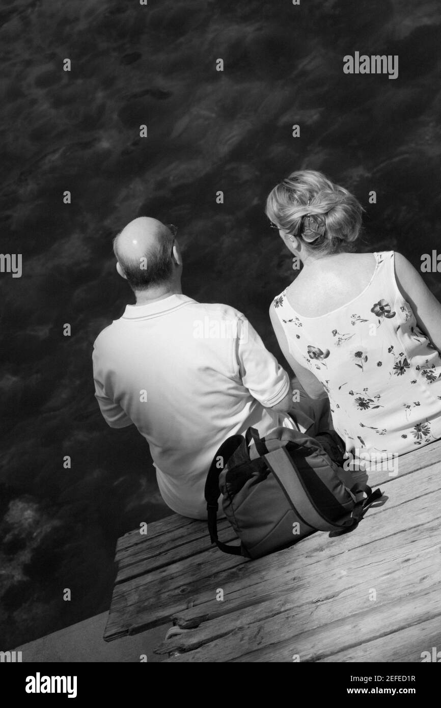 Vista posteriore di una coppia seduta su una passerella, Baia di Napoli, Sorrento, Penisola Sorrentina, Provincia di Napoli, Campania, Italia Foto Stock
