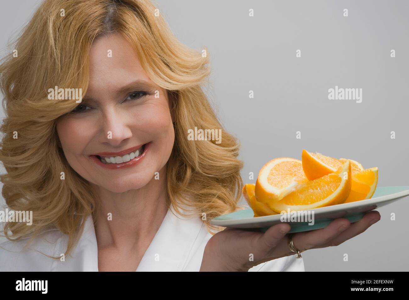 Ritratto di una donna matura che tiene un piatto di arance e sorridendo Foto Stock