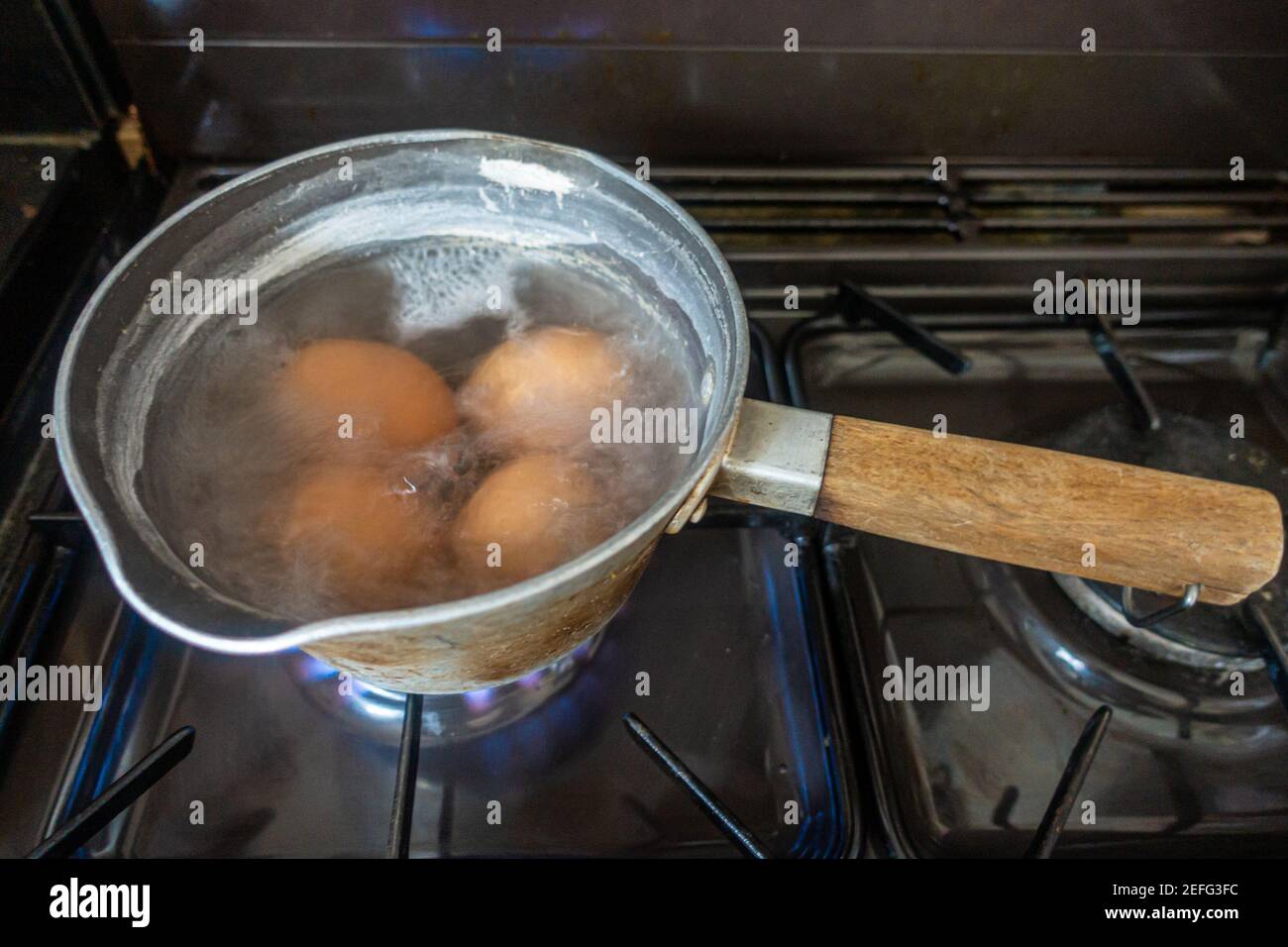 Uova cucinando in una padella di acqua bollente su un piano cottura a gas. Foto Stock