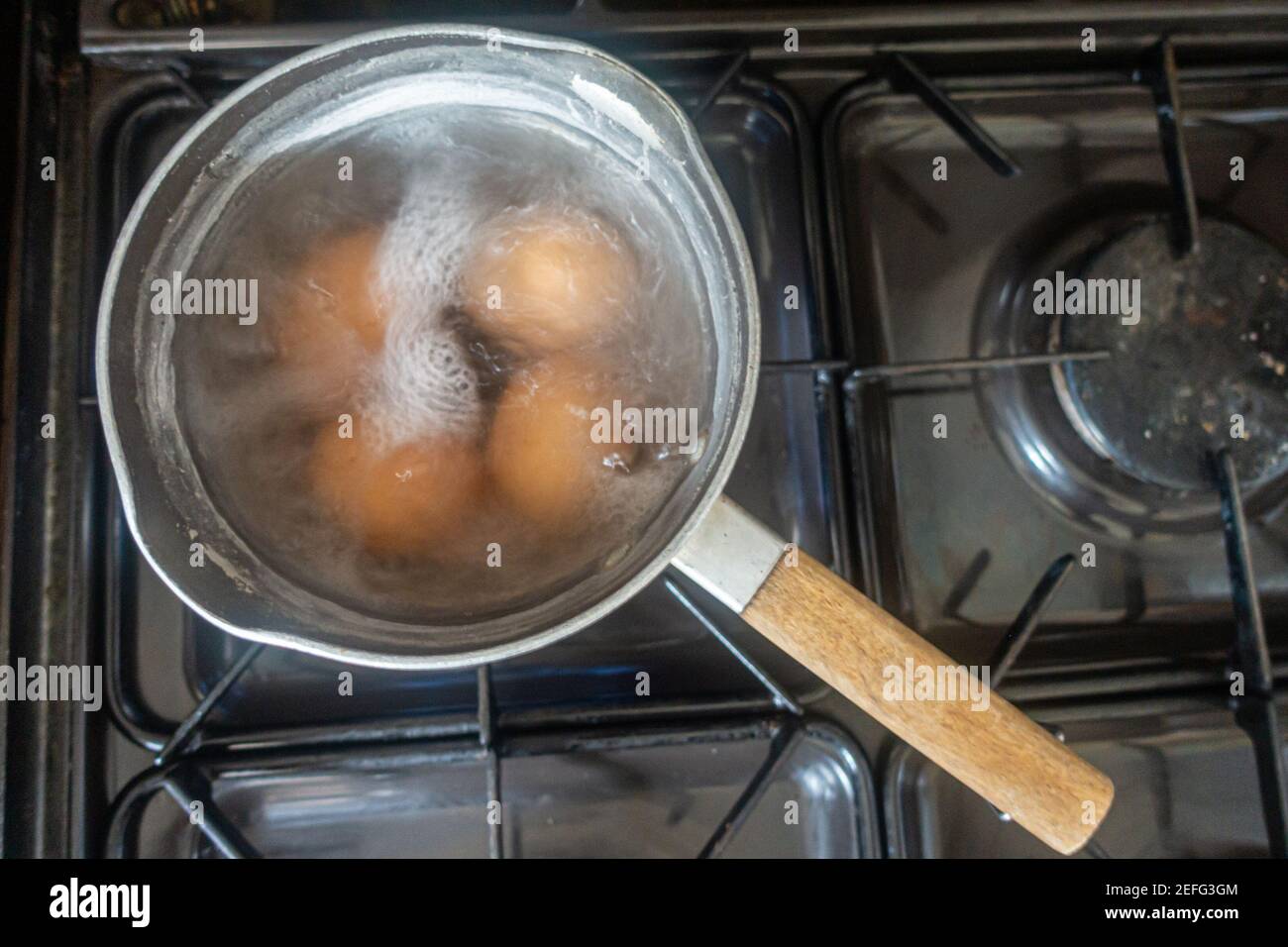 Uova cucinando in una padella di acqua bollente su un piano cottura a gas. Foto Stock