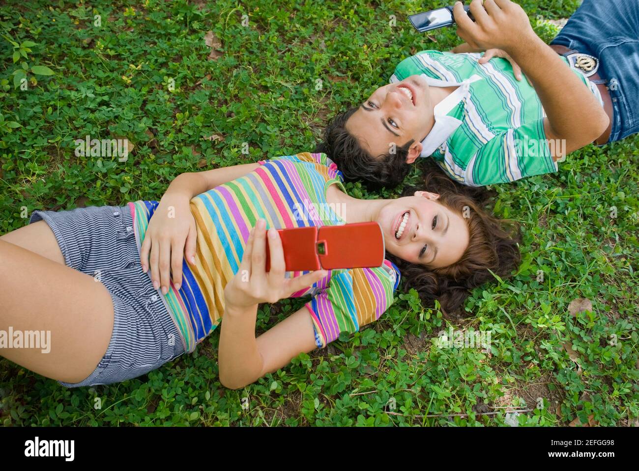Angolo di alta vista di una giovane coppia giacendo in posizione di parcheggio e in possesso di un telefono cellulare Foto Stock