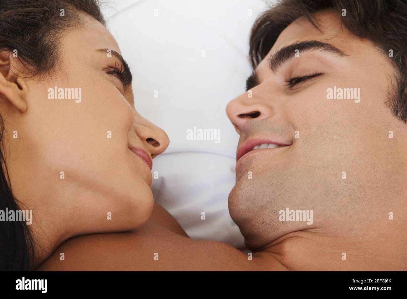 Primo piano di una giovane coppia sdraiata sul letto guardando l'uno all'altro Foto Stock