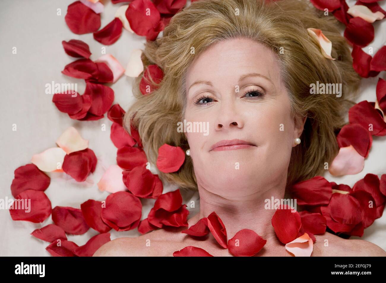 Ritratto di una donna matura sdraiata su un tavolo da massaggio con petali di rosa sul suo corpo Foto Stock