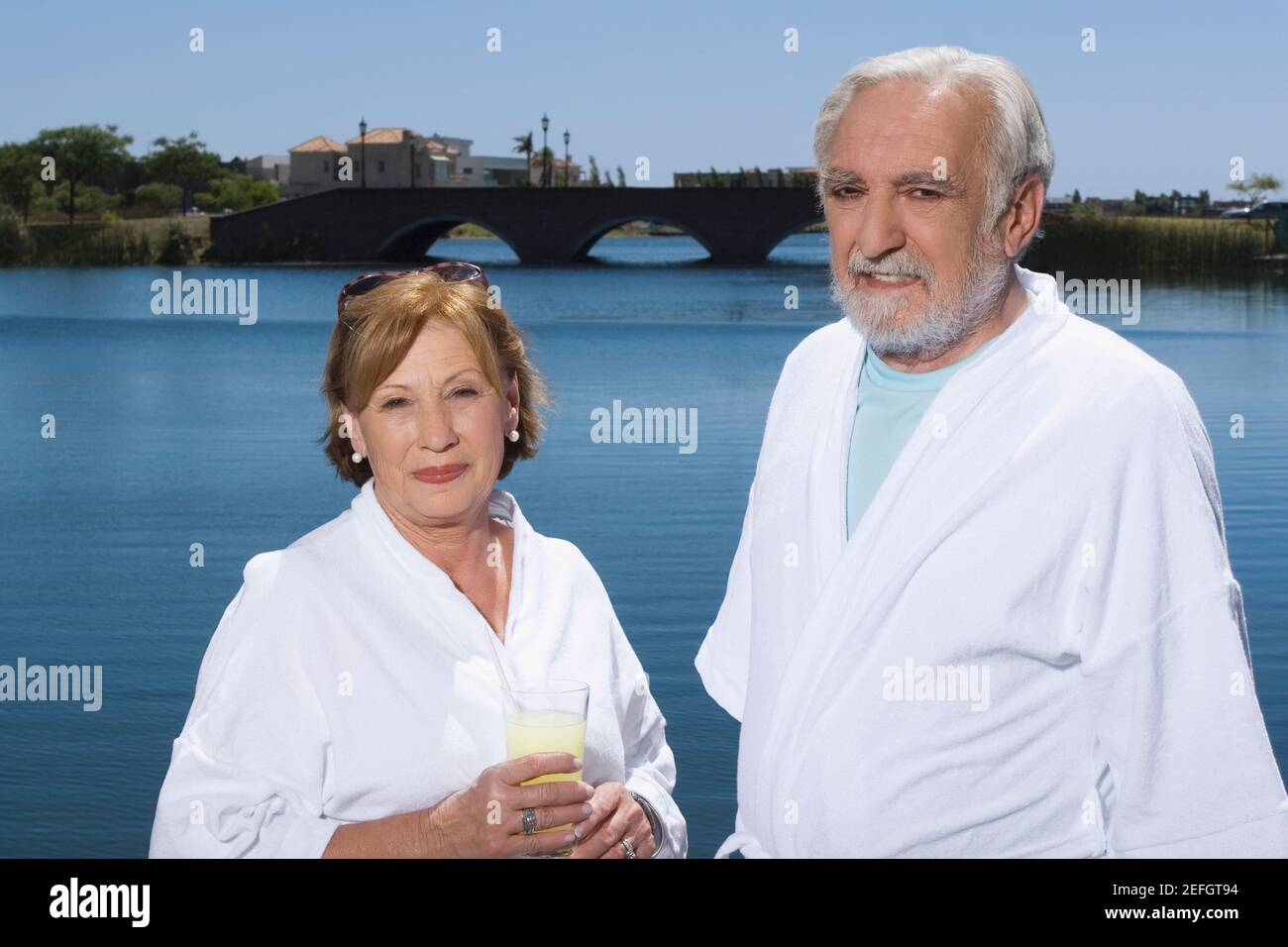 Donna anziana che tiene un bicchiere di succo e sta con un uomo anziano Foto Stock