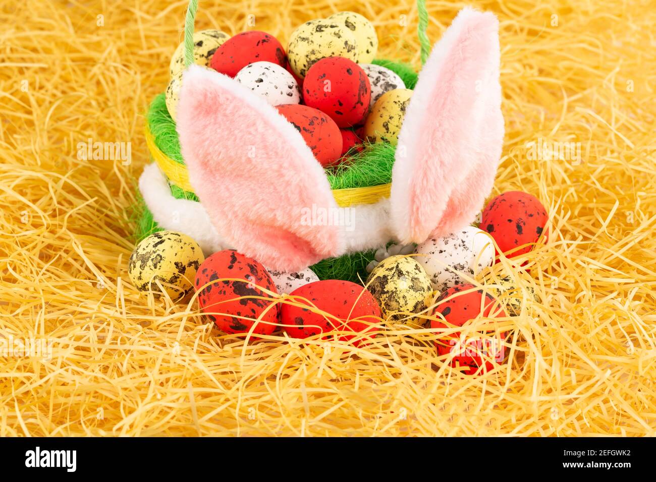 Pasqua uova colorate in cesto e spighe rosa coniglietto su sfondo giallo paglia. Foto Stock