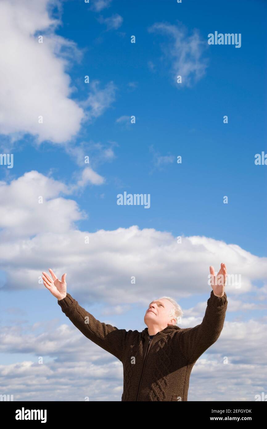 Vista ad angolo basso di un uomo anziano in piedi con il suo bracci sollevati Foto Stock