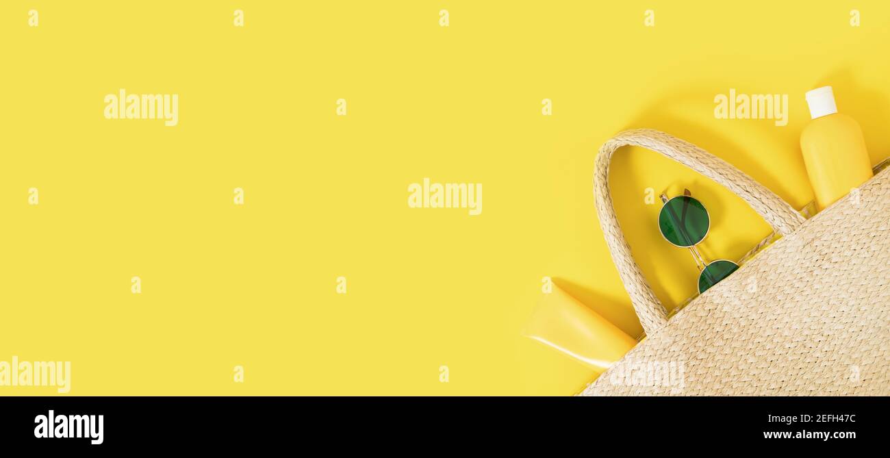 Banner giallo estivo flatlay su sfondo colorato con sacco di paglia in vimini, tubi e bottiglia con crema solare, occhiali da sole verdi. Ombre e luci dure. Foto Stock