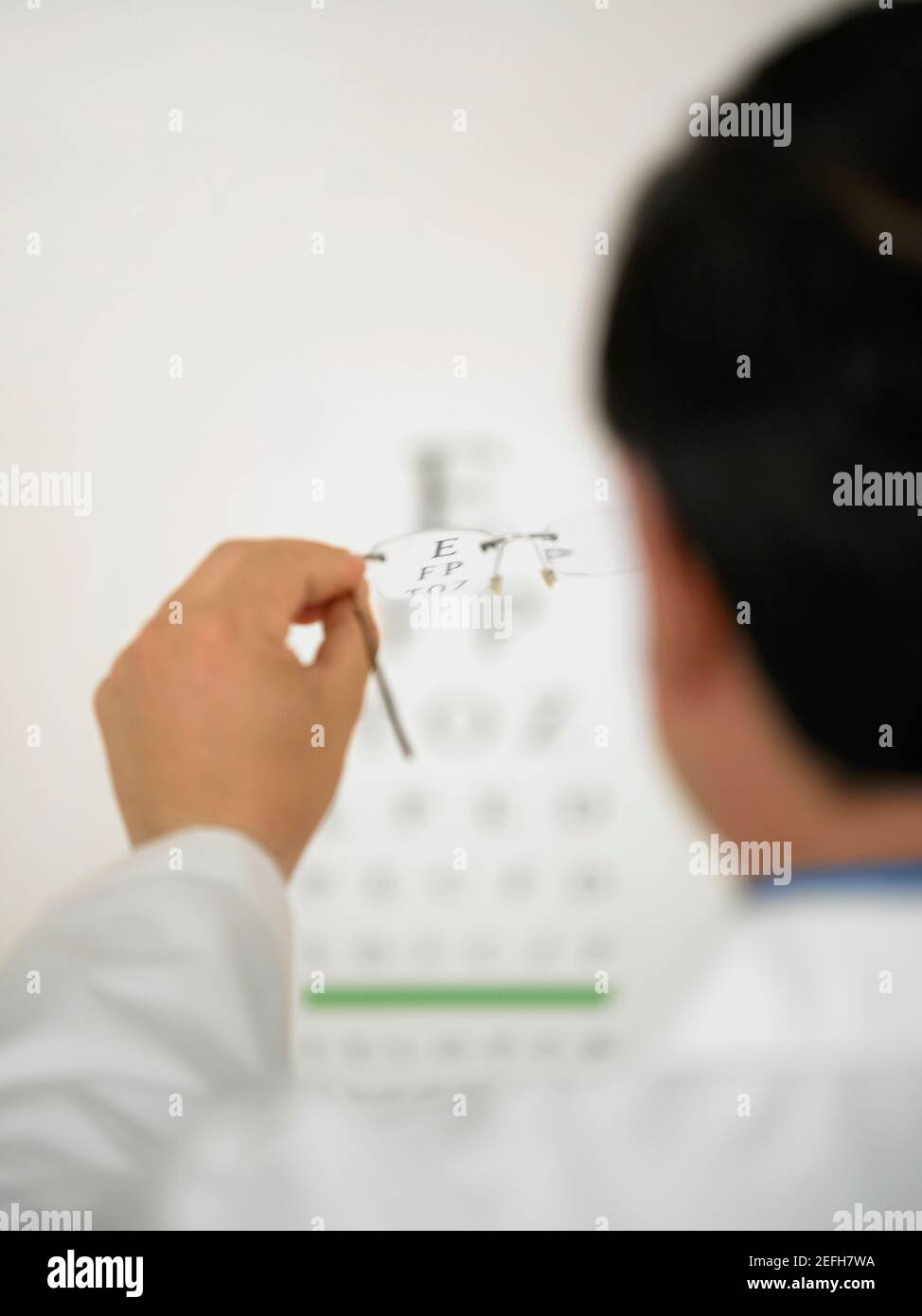 Vista posteriore di un medico che tiene un paio di occhiali Foto Stock