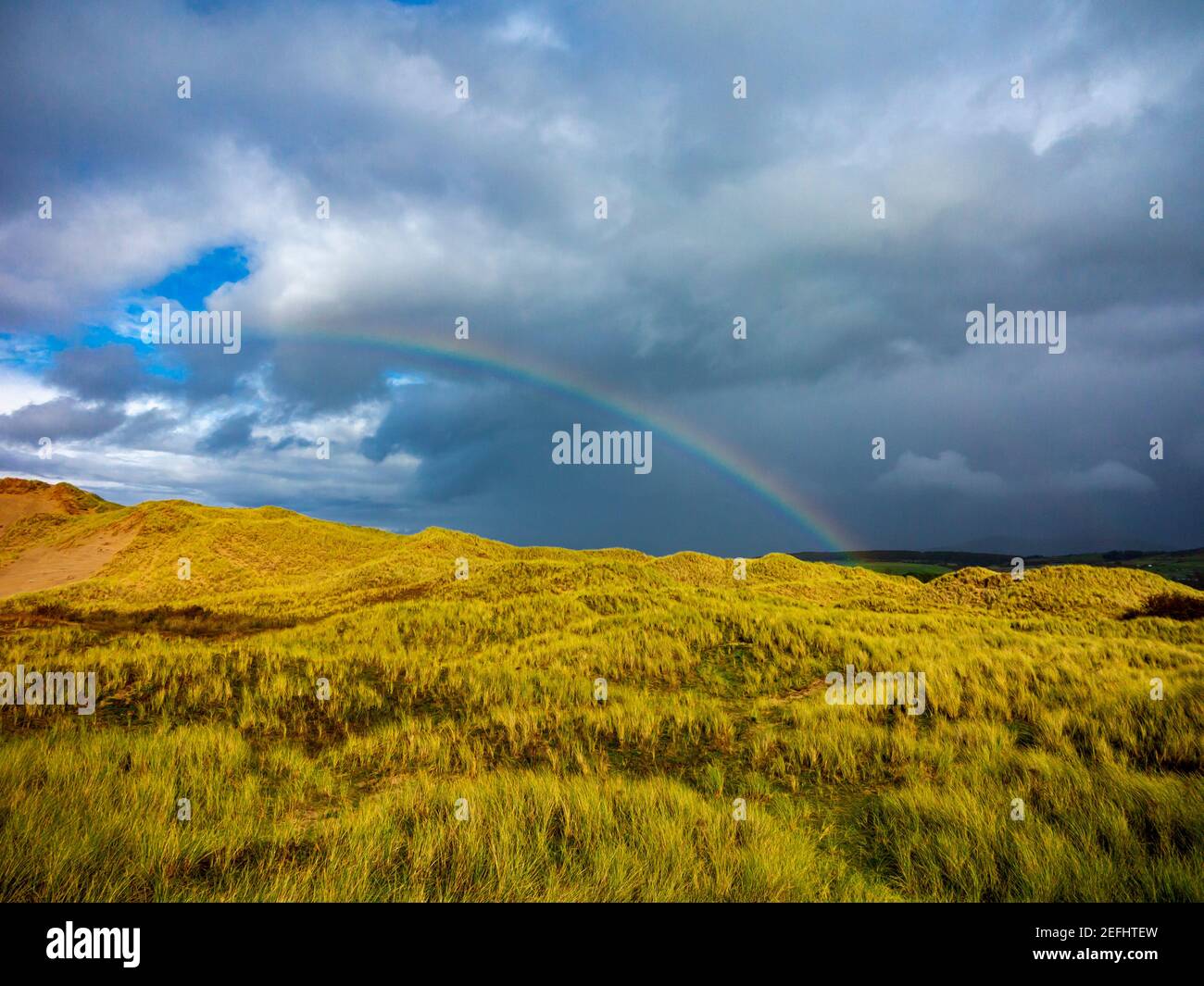 Dune di sabbia dietro la spiaggia di Morfa Dyffryn tra Barmouth e Harlech a Gwynedd sulla costa nord-occidentale del Galles con cielo tempestoso e arcobaleno sopra. Foto Stock