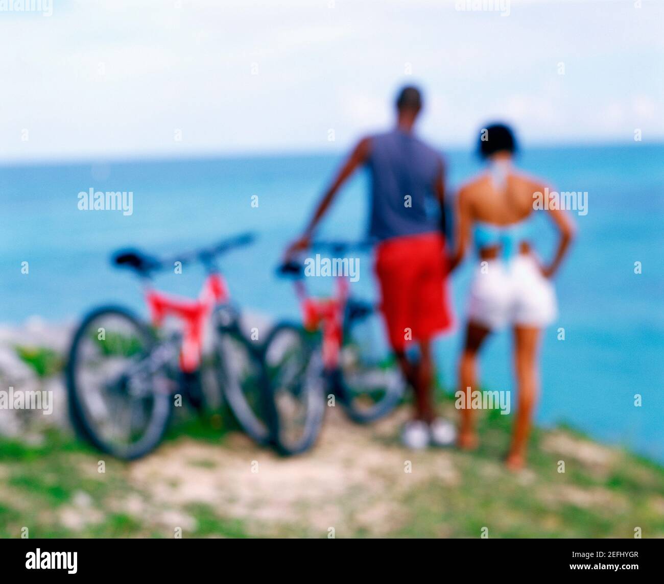 Vista posteriore di una giovane coppia in piedi con biciclette sulla costa, Bermuda Foto Stock