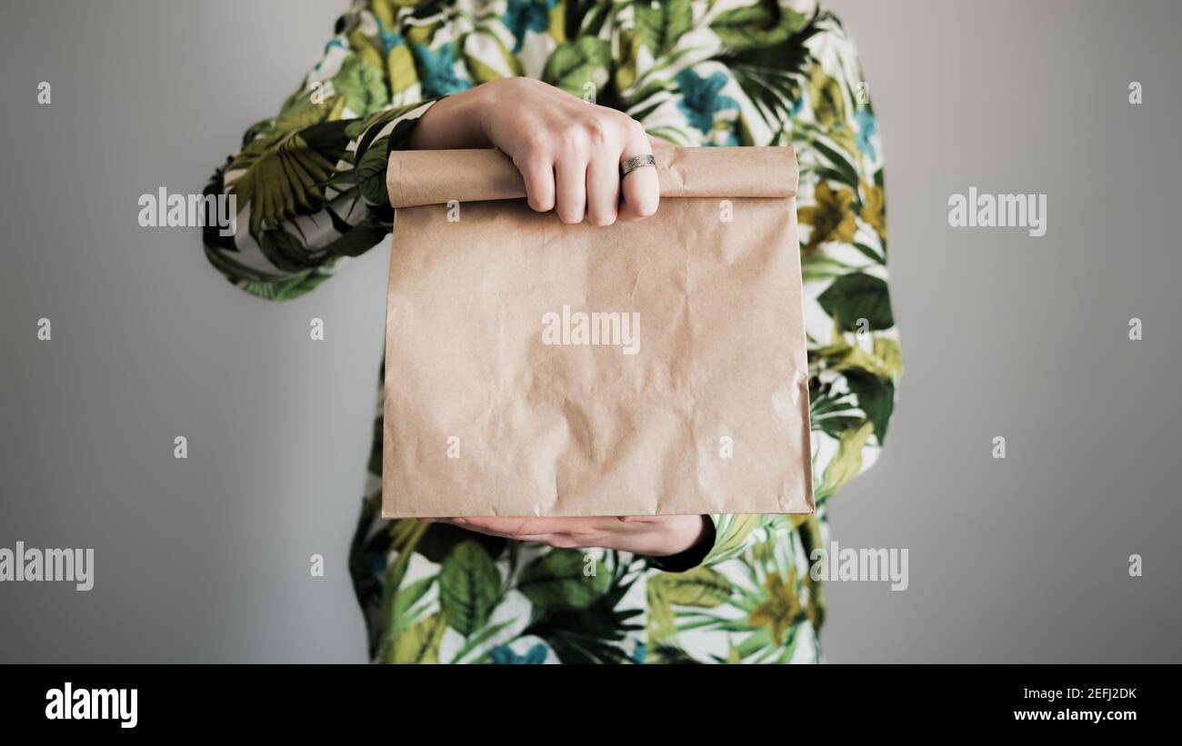 Mano femmina tenere un sacchetto di carta marrone, primo piano. Pacchetto ecologico vuoto, regalo, sorpresa o concetto di consegna Foto Stock