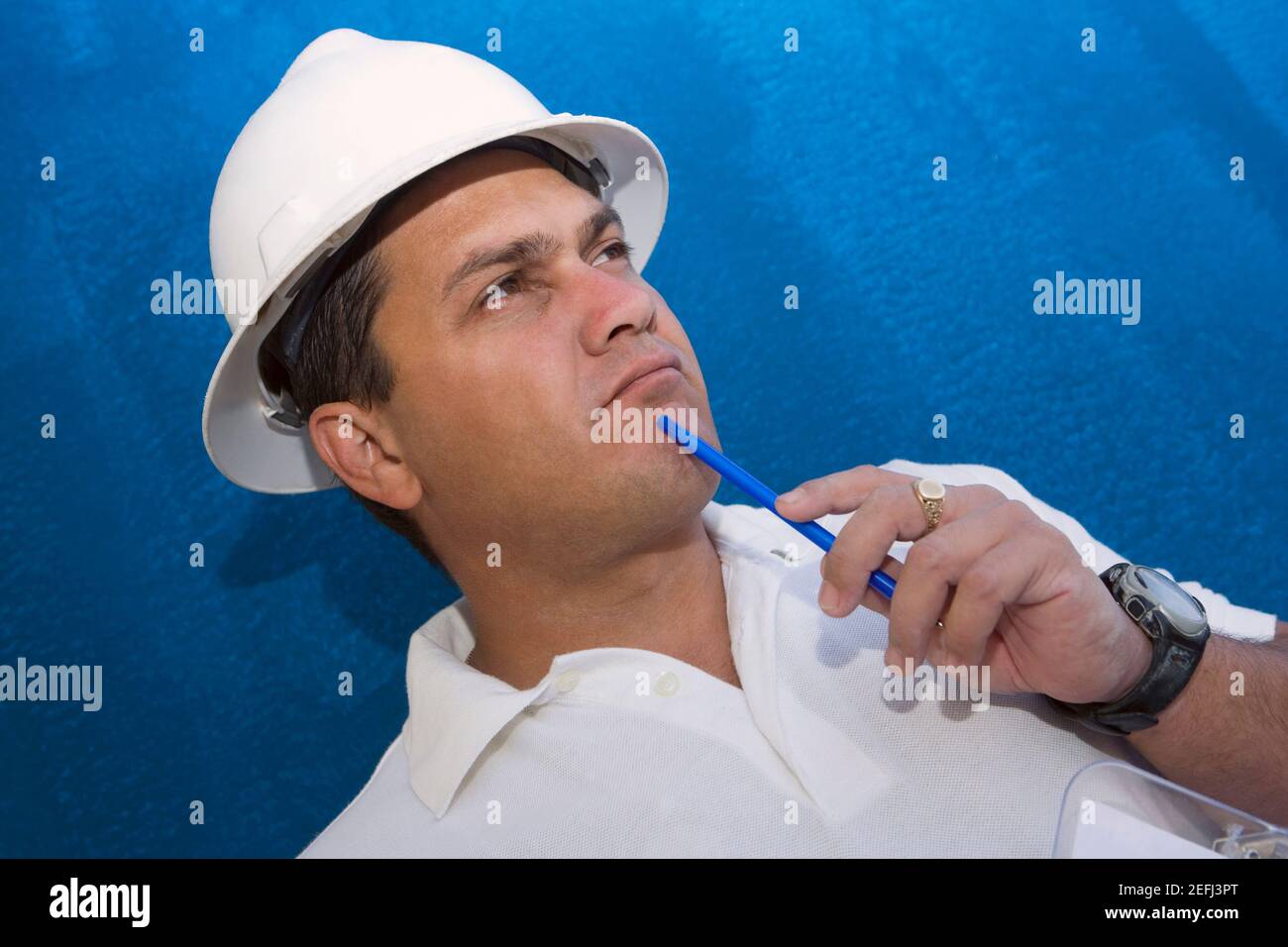 Primo piano di un lavoratore di costruzione maschile che tiene una penna e. pensare Foto Stock