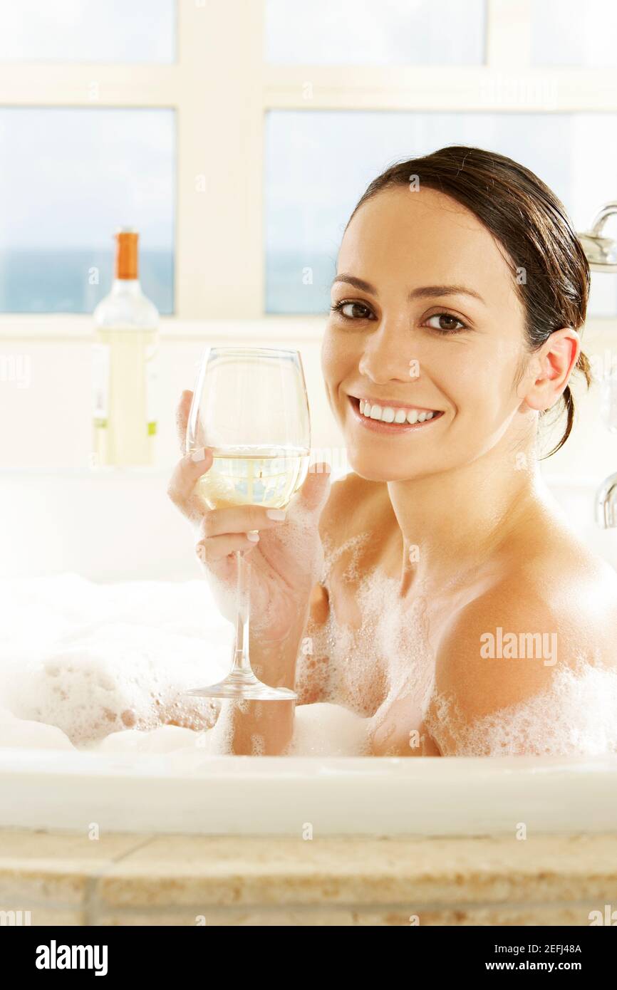 Profilo laterale di una giovane donna che tiene un bicchiere di vino nella vasca da bagno Foto Stock
