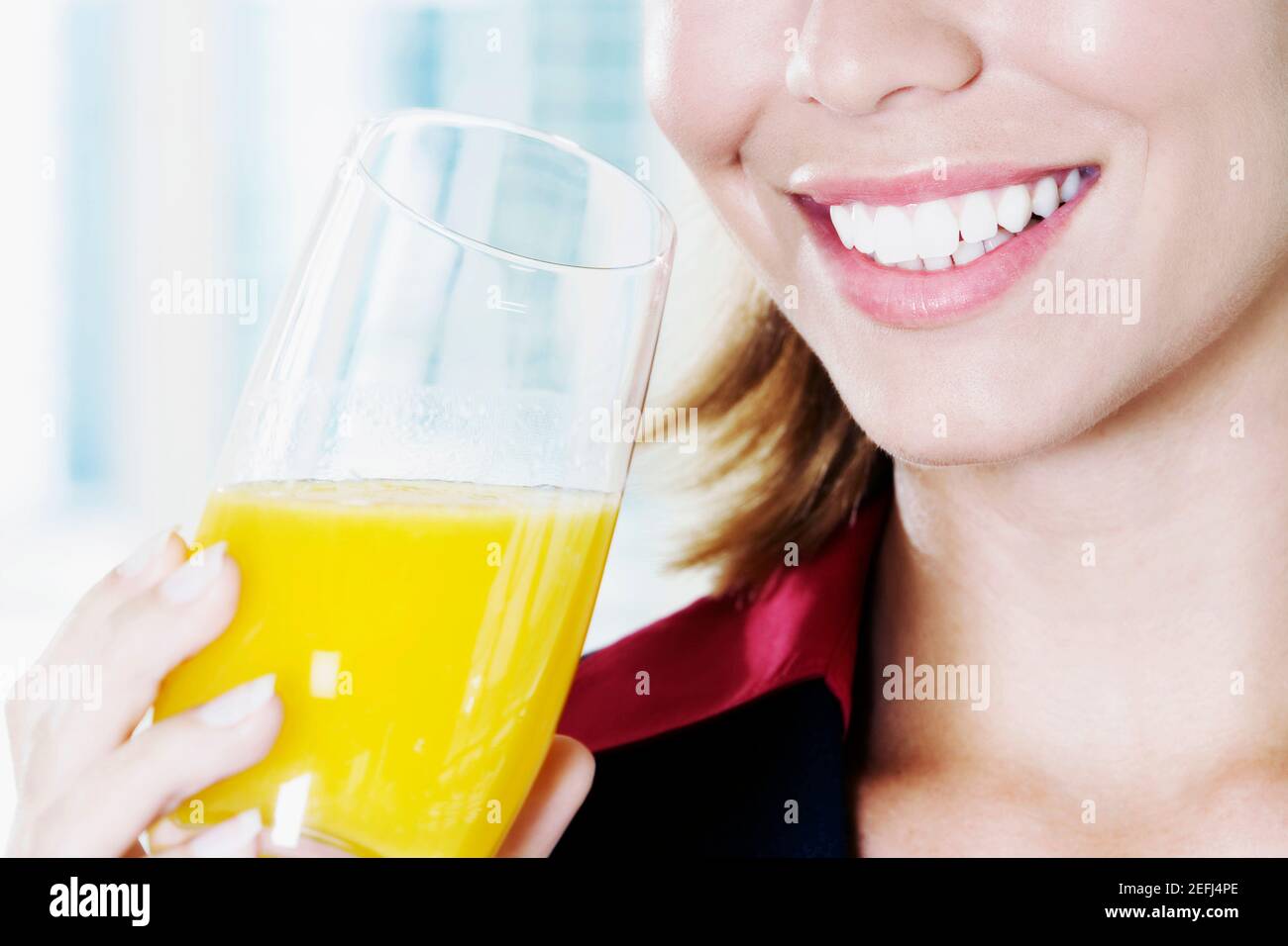 Primo piano di una giovane donna che tiene un bicchiere di arancio succhi e sorridenti Foto Stock