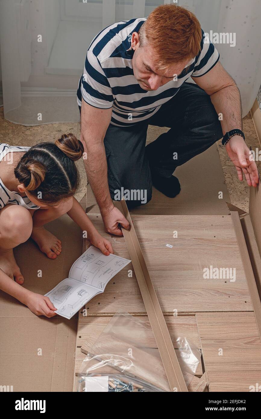 Un padre e la sua bella figlia studiano insieme le istruzioni per l'assemblaggio di nuovi mobili. I valori della famiglia e il tempo trascorso insieme. Ver Foto Stock