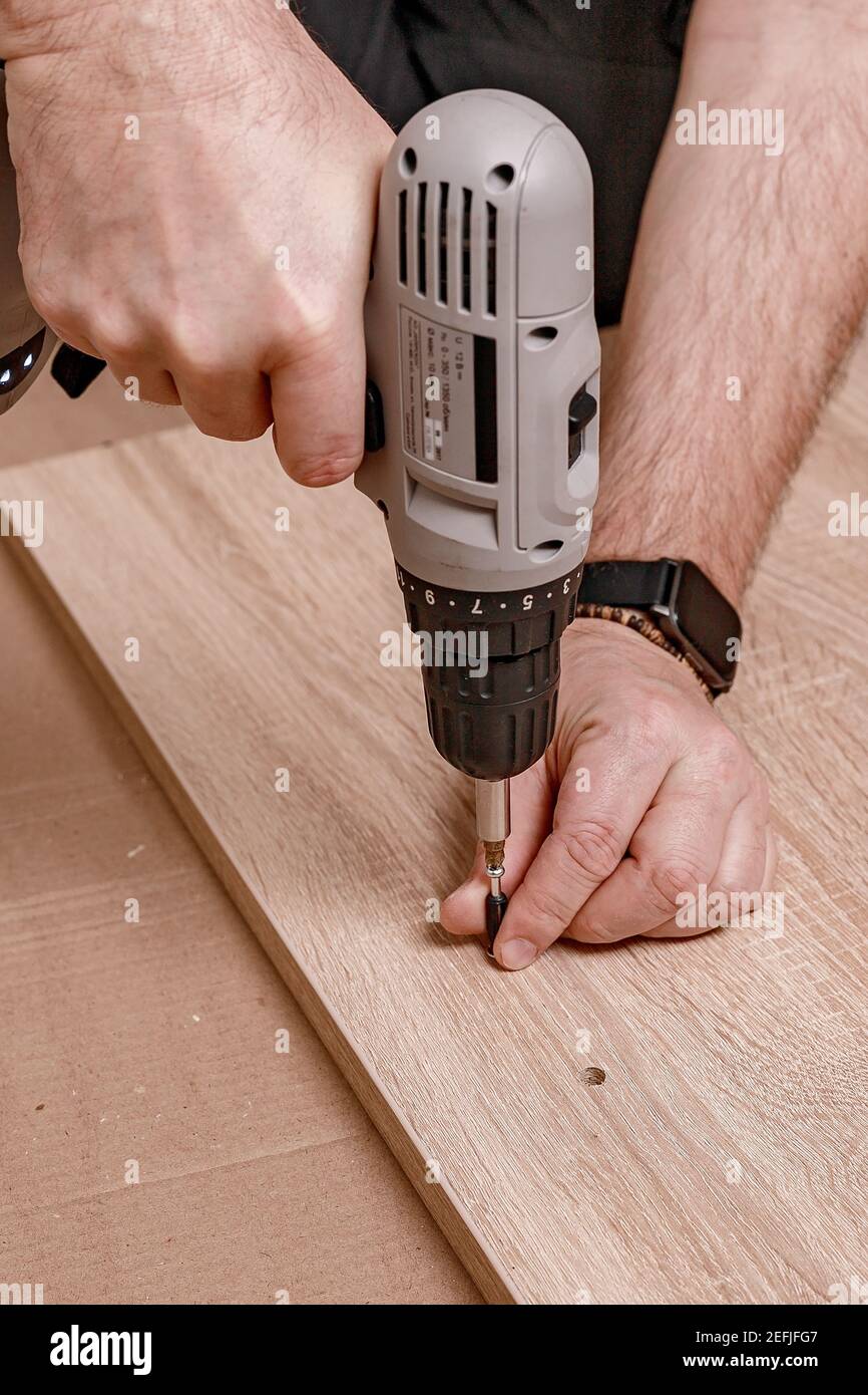 Mano caucasica mans che tiene un cacciavite elettrico. L'uomo assembla i mobili a casa. Lavori domestici. Primo piano. Shot verticale Foto Stock