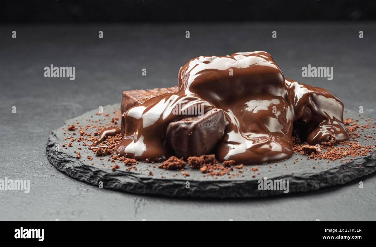 Caramelle ricoperte di cioccolato, caramelle con cioccolato fuso su sfondo nero Foto Stock