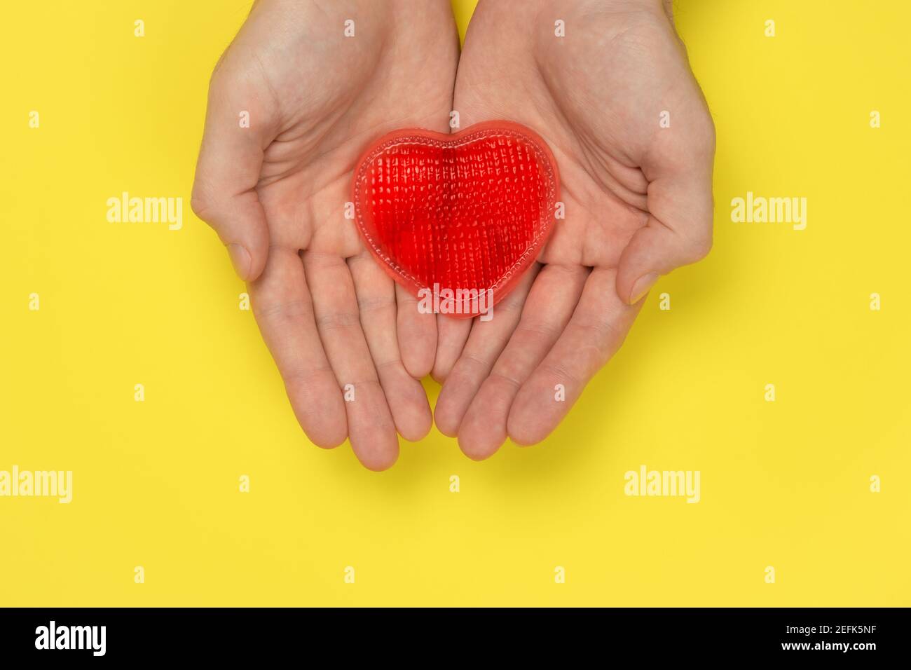 Le mani degli uomini stanno tenendo un cuore rosso su uno sfondo giallo. Amore, concetto di relazione. Simbolo romantico, buono regalo per San Valentino Foto Stock