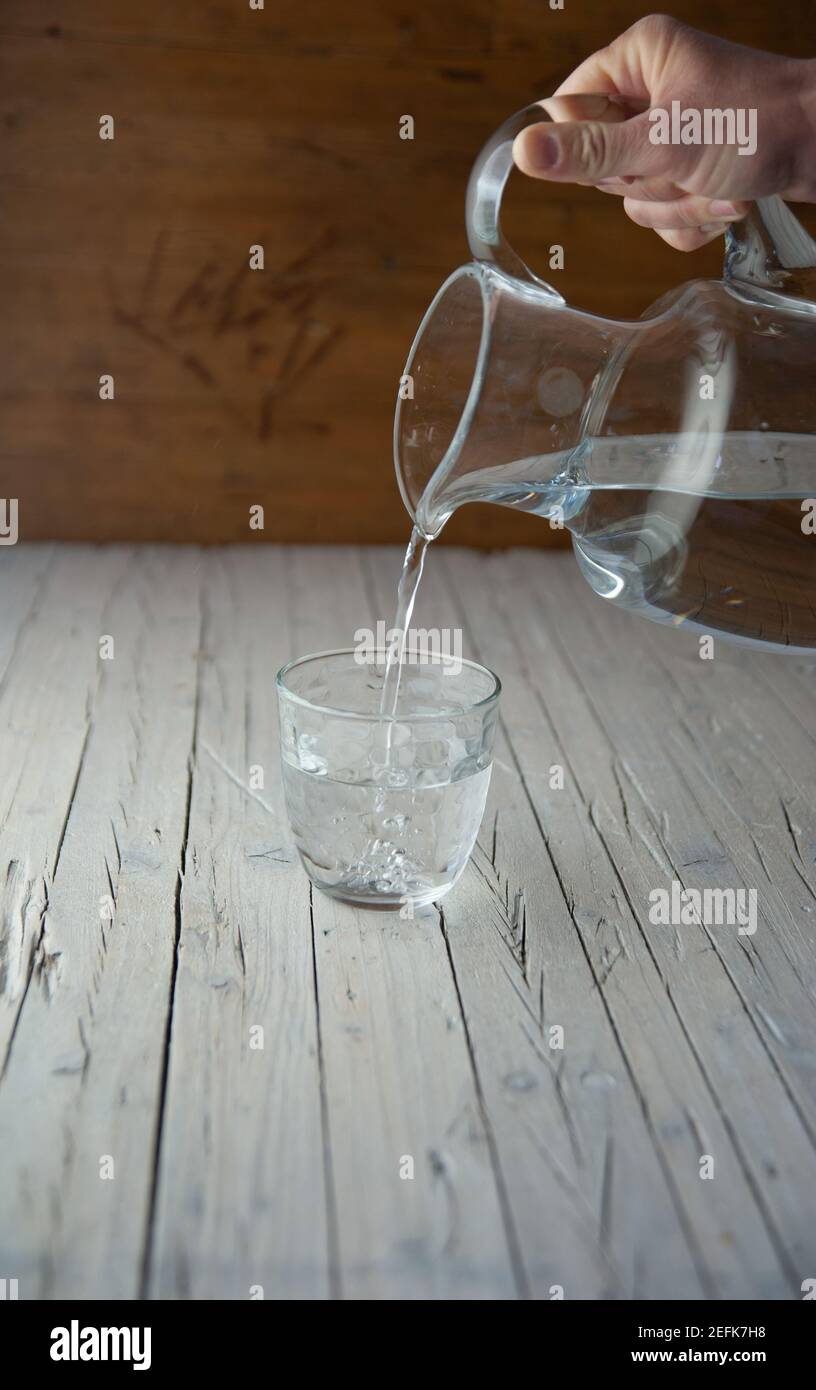 la mano versa una caraffa d'acqua in un bicchiere di vetro Foto Stock