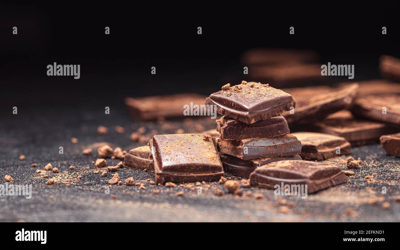 Barrette di cioccolato su sfondo di ardesia nera con polvere di cacao Foto Stock Barrette di cioccolato su sfondo di ardesia nera con polvere di cacao Foto Stock