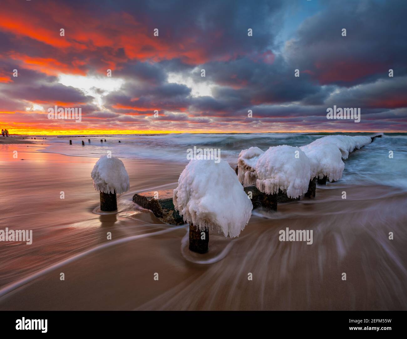 Bellissimo paesaggio invernale del mare. Frangiflutti di ghiaccio, onde e tramonti ardenti. Fotografia artistica. Foto Stock