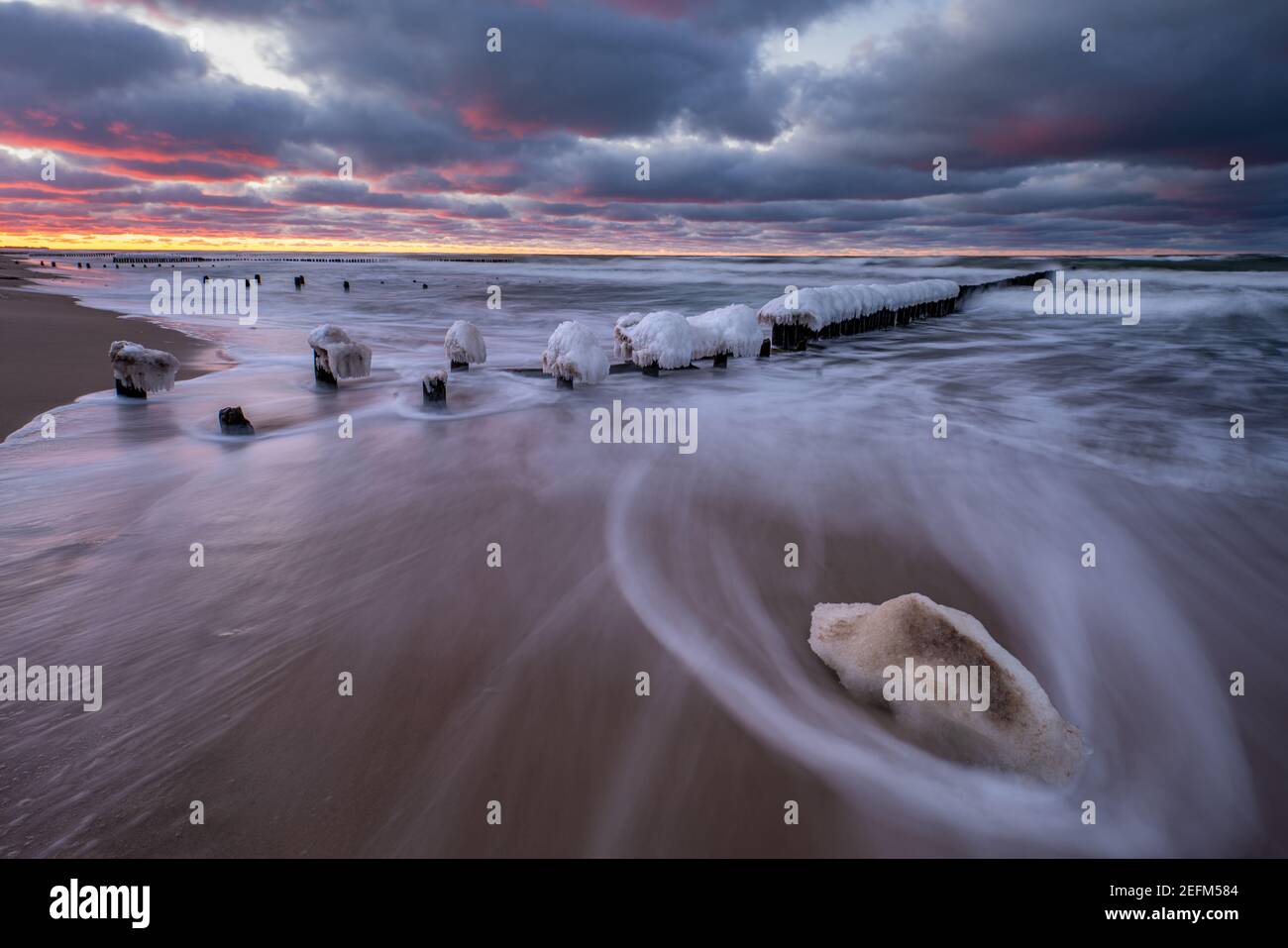 Bellissimo paesaggio invernale del mare. Frangiflutti di ghiaccio, onde e tramonti ardenti. Fotografia artistica. Foto Stock