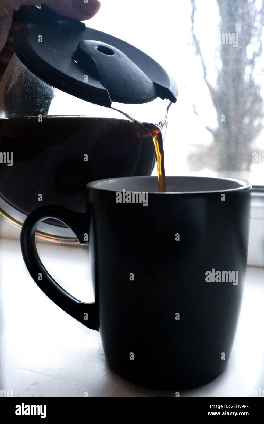 qualcuno versa il caffè scuro in una tazza nera Foto Stock