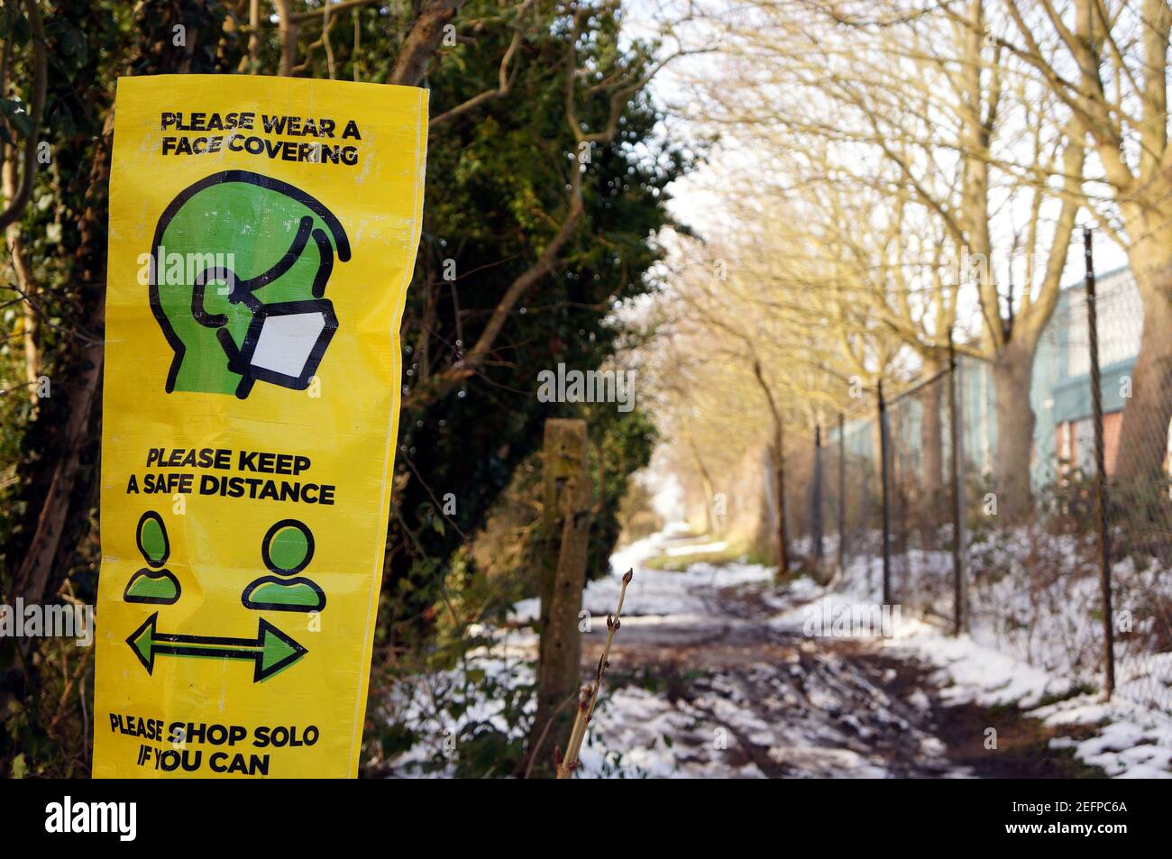 Un cartello di avvertenza COVID 19 giallo e verde su un tracciato innevato. Foto Stock