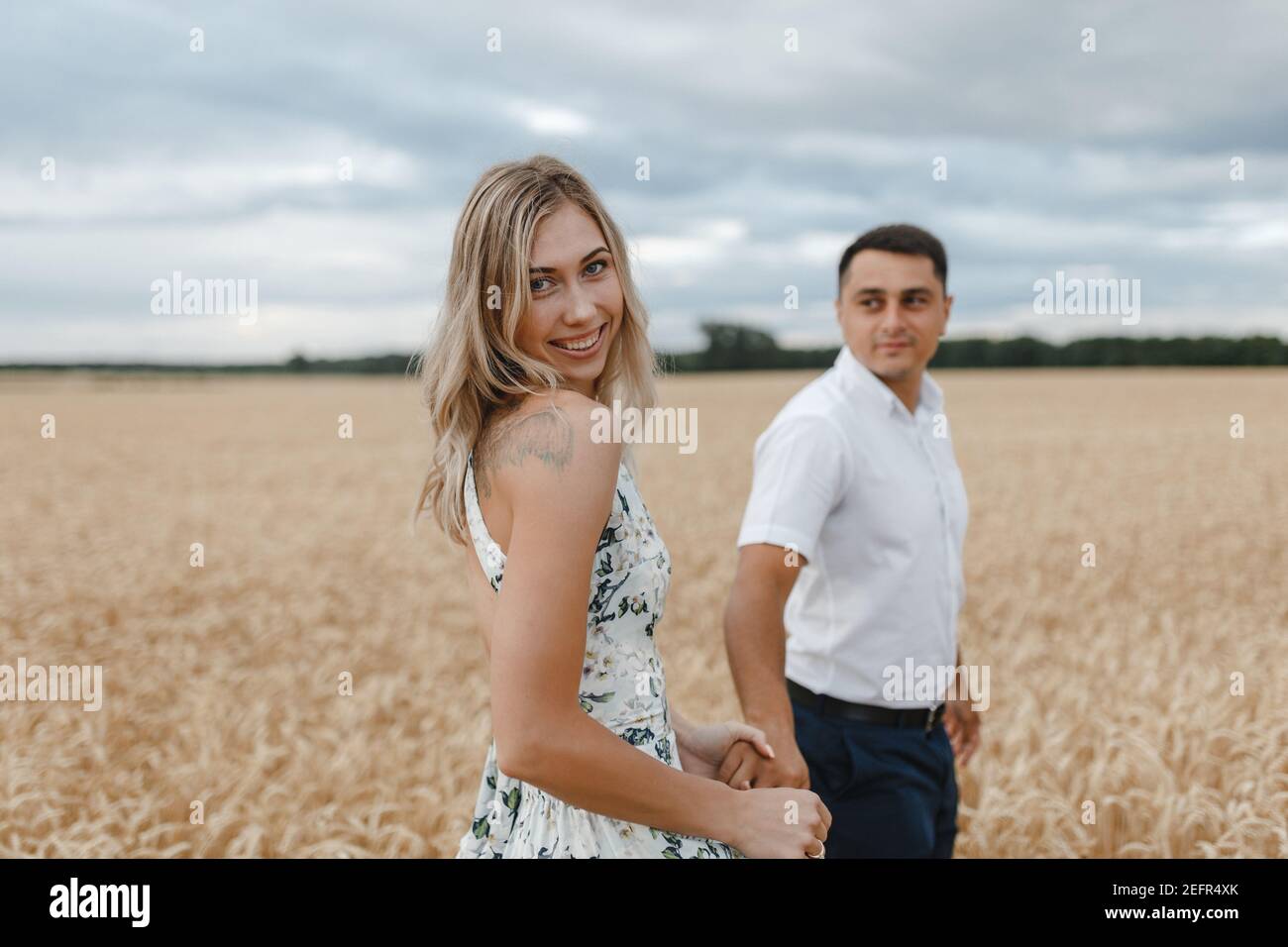 Coppia sorridente in piedi in un campo di grano e tenendo le mani. Uomo che guarda la sua donna sul campo. Amanti del grano. Foto Stock