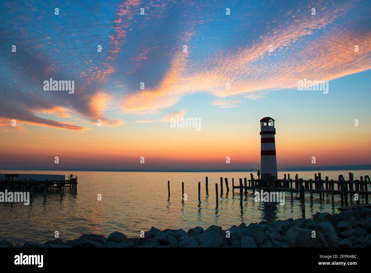 Il cielo del tramonto sopra il paesaggio dell'orizzonte del mare con il faro simbolo con le colonne di legno del molo in piedi in acqua, vista panoramica al crepuscolo dal molo di P. Foto Stock