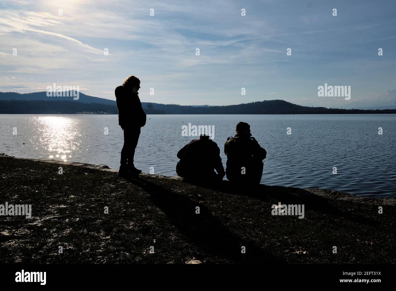 madre con due bambini, seduta sul bordo di un lago alpino, guarda il tramonto Foto Stock