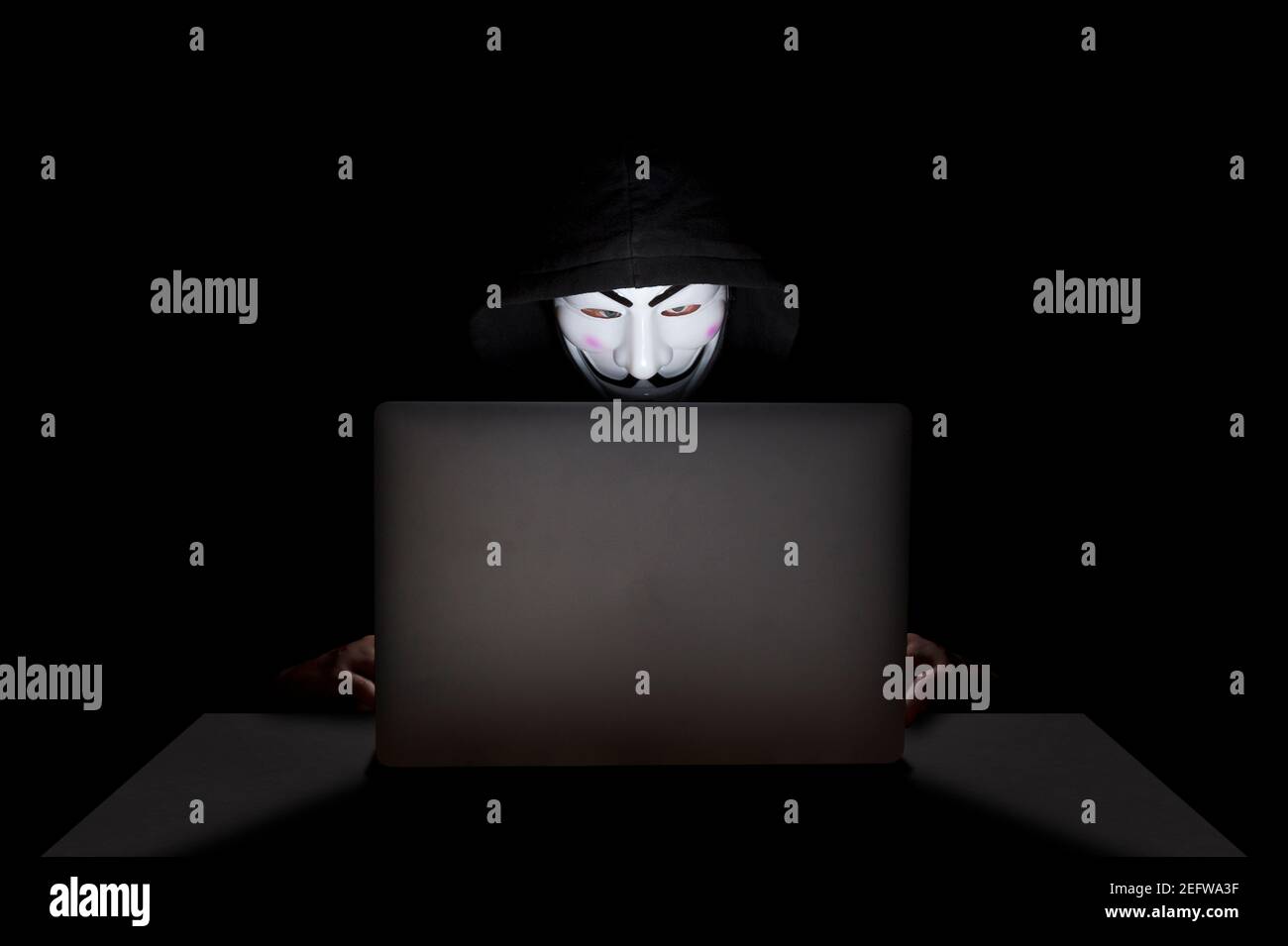 Membro del gruppo di hacker anonimi che indossa una maschera davanti al suo laptop mentre commette un hack. Foto Stock
