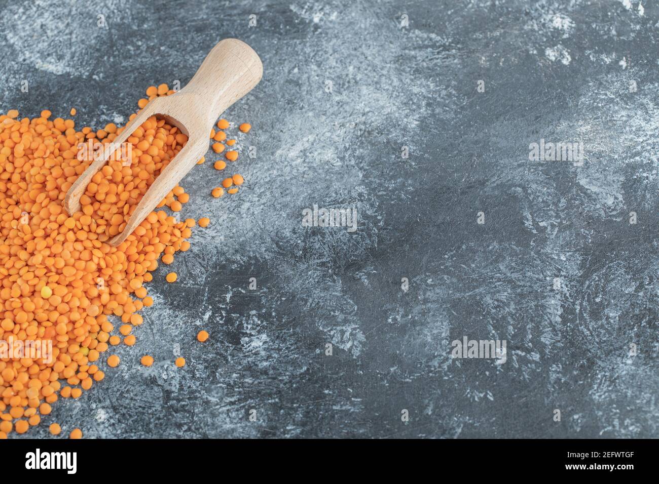 Un cucchiaio di legno pieno di lenticchie grezze su un grigio sfondo Foto Stock